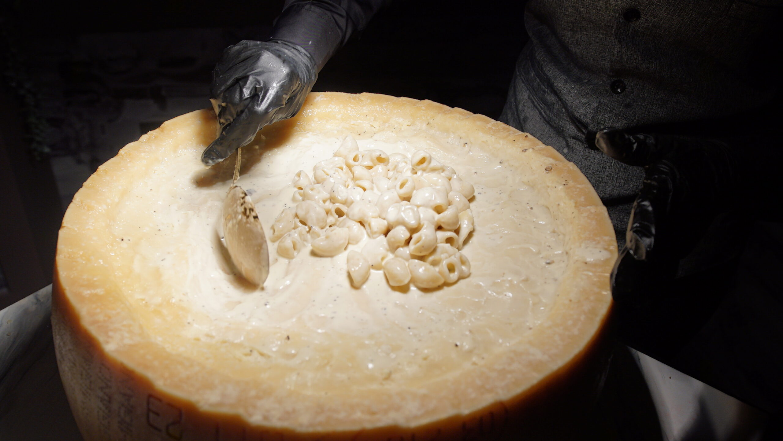 kpacho-italian-station-cheese-wheel Chef scraping melted cheese from an artisanal cheese wheel at K. Pacho's Italian Station